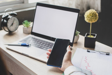 Blank screen laptop with hand of woman holding blank screen smart phone. Mockup screen for Ads. Advertising concept on a screen. Empty copy space on monitor for advertisement