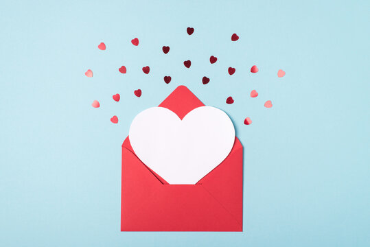 Valentine day invitation congratulation concept. Flat lay layout top view close up view photo of open red envelope with blank paper card inside and flying confetti isolated pastel blue backdrop