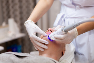 A young beautiful girl lies on the beautician's table and receives procedures with a professional apparatus for skin rejuvenation and moisturizing