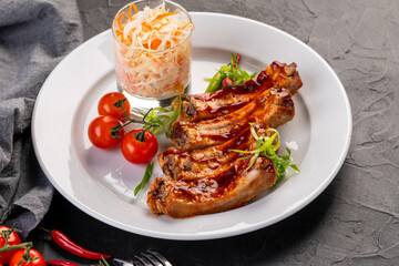 grilled ribs in barbecue sauce with cabbage salad and cherry tomatoes in white plate