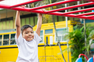 Obraz premium Kid exercise for health and sport concept. Happy Asian student​ child boy playing and hanging from a steel bar at the playground. 6-7 years old.