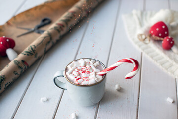 Christmas cocoa with candy cane, marshmellow and falling red sugar on white wooden background surrounded by new year entourage. Christmas greeting card. Frozen motion