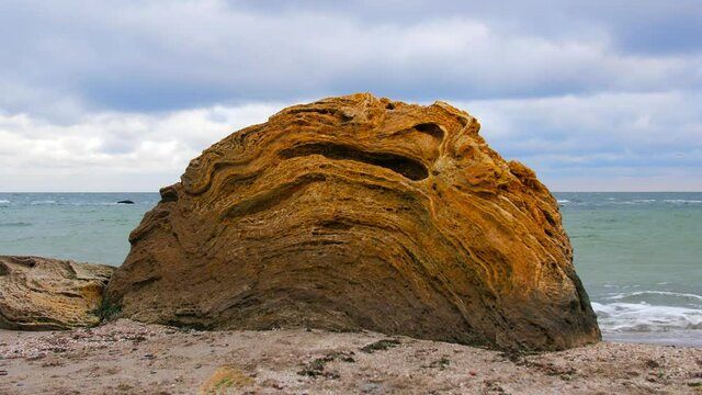 Big coquina rock on the coast with sea waves on the background. Cloudy weather. 4K.