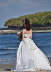 Fototapeta na wymiar 海辺で花束を持っているウエディングドレスの女性