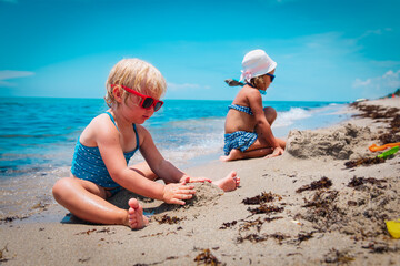cute little girls play with sand on beach