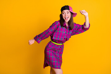 Photo of cheerful funny brunette girl dancing hands fists wear pink dress headwear isolated on yellow color background