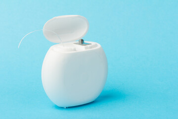 Dental floss container on blue background. Daily oral hygiene, teeth care and health. Cleaning products for your mouth, copy space. Dental care concept.