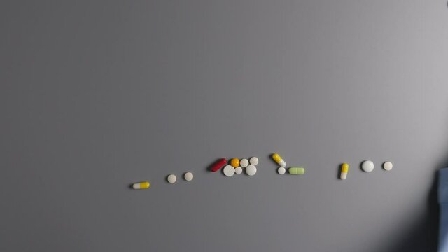 Hand in blue medical protective glove swipe away sign COVID made of pills, tablets and capsules from gray table