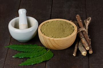 neem powder in wooden bowl with neem leaf and white mortar and pestle on wooden background.