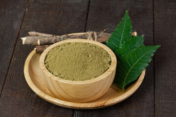 neem powder in wooden bowl with neem leaf and stick on wooden background.