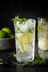 Glass of iced lemonade with lime and mint, cold summer drink on dark background
