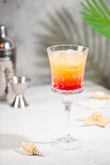 Colourful exotic Tequila Sunrise cocktail in a glass served with ice on gray background