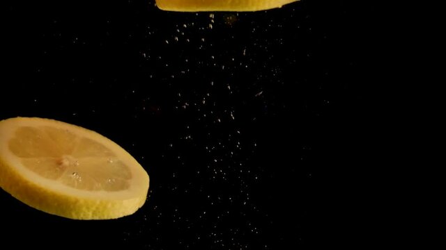 lemon slices falling, drop into water with air bubbles and a smooth black background. perfect for advertising or commercial videos for lemonade or juice. Also perfect for  baar and drinks