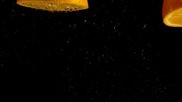 Orange halves falling, drop into water with air bubbles and a smooth black background. perfect for advertising or commercial videos for lemonade, juice and cocktails Also perfect for  baar and drinks