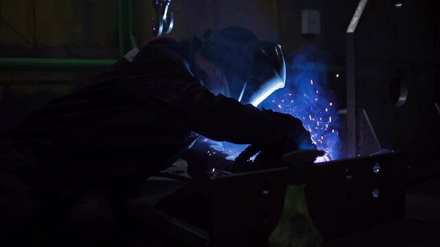 Professional worker in mask welds parts at factory. Clip. Welder in overalls works at factory. Welding of metal parts in factory