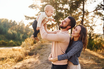 Happy family of mother, family and little baby rests outdoors. Beautiful sunny autumn nature