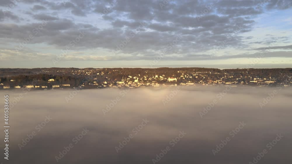 Wall mural The drone flies to Starnberg, a tourist town near Munich in Bavaria. Lake Starnberg is covered by fog at sunrise. Aerial view through the clouds