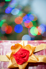 A gift tied with a golden ribbon with a red bow. Gift box with a bow. A gift at Christmas. Shiny Christmas tree lights in the background.