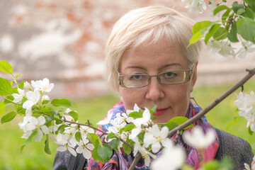 Portrait of mature blonde short haired woman among apple blossoms