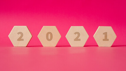 four wooden hexagonal shapes with numbers of new year 2021 stand against a background of pink paper