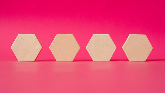 four wooden hexagonal shapes stand against a background of pink paper - Powered by Adobe