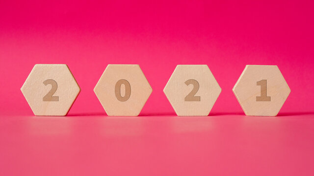 four wooden hexagonal shapes with numbers of new year 2021 stand against a background of pink paper