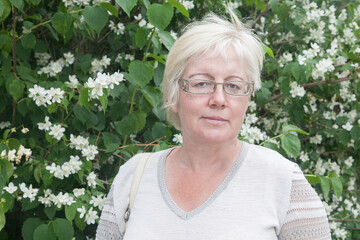 Mature blonde short haired woman in linen clothes near jasmine flowers