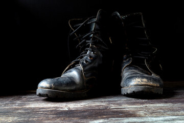Old and torn black boots. Fashion shoes placed on black wooden floor