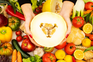 A close up on a girl's hands holding a melon on a kitchen table with vegetables
