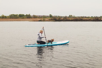 Girl swims on a SAP board with a dog. Walk on the lake near the spring pine forest.