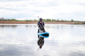 Man swims on a SAP board with a husky dog. Walk on the lake near the spring pine forest.