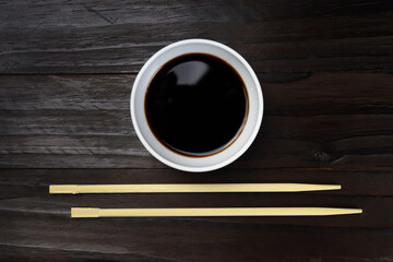 Wooden chopsticks, sushi sticks and saucepan with sauce on a dark background