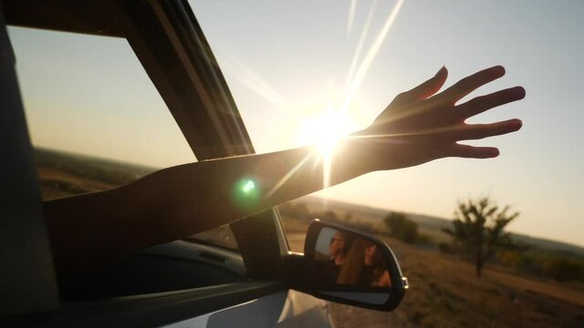 free girl hand out of the window rides a car wind in the face. concept car travel on the road. girl stretches her hand out of the car window sun glare sunset. driver hand movement out of the window