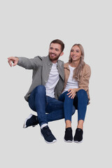 Fototapeta premium Couple Sitting on Floor Man Pointing to Side. Couple Isolated Watching Front. Relationship, Family, Lovers, Friends Concept