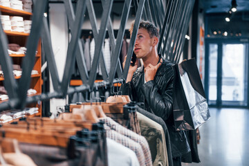 Fototapeta na wymiar Talks by the phone. Young guy in modern store with new clothes. Elegant expensive wear for men