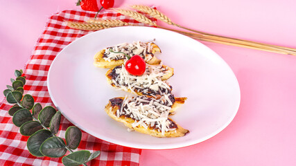 Pisang Kepok Bakar (grilled banana) served with chocolate and cheese on pink background