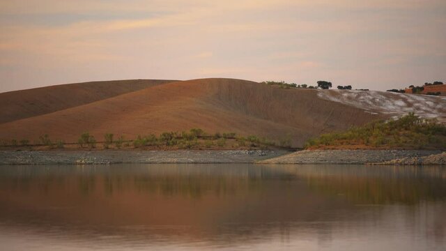 Desert like hill landscape with reflection on the water on a dam lake reservoir at sunset in Terena, Portugal