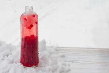 A bottle of red currant juice is cooled in the snow in winter. © Olga