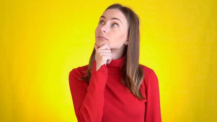 Young woman isolated on yellow background in studio. People sincere emotions, lifestyle concept. Looks at camera, thinks, scratches at temple comes up with ideas