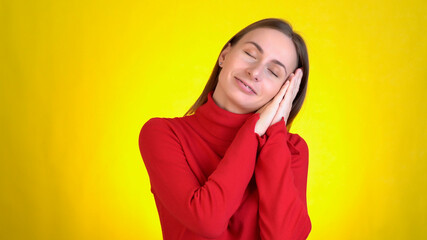 Tired cute woman yawning sleep with folded hands under cheek watching dreams isolated on yellow background studio. 