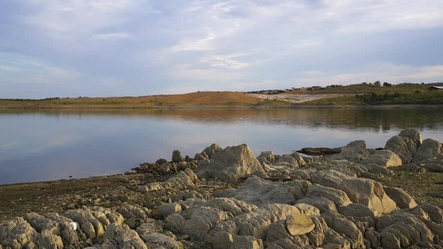 Lucefecit Dam in Terena with reflection on the lake reservoir and rocks on the foreground, in Portugal