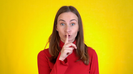 Young woman posing isolated on yellow background studio. People lifestyle concept. Looking aside say hush be quiet with finger on lips gesture