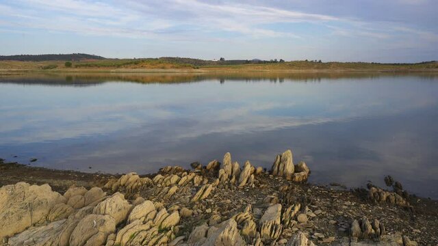 Lucefecit Dam in Terena with reflection on the lake reservoir and rocks on the foreground, in Portugal
