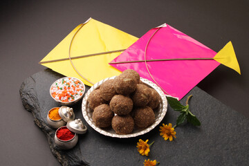 Til Gul OR Sweet Sesame Laddu with Kite model, haldi Kumkum and sugar crystals for Makar Sankranti festival over black background.