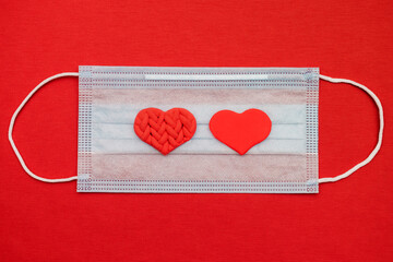 Two red hearts on a medical protective mask on a red background.Valentine's day background.New normal concept.Flat lay, copy space, top view.