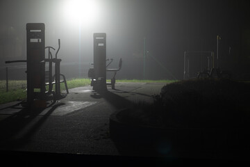 Dead of night, outdoor gym abandoned and spooky place, illuminated by street lamp from behind