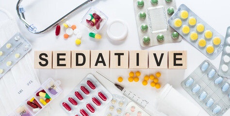 SEDATIVE medicine word on wooden blocks on a desk. Medical concept with pills, vitamins, stethoscope and syringe on the background.
