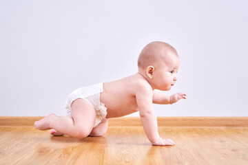 Toddler boy in a diaper learns to crawl on the floor at home