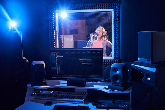 Professional male sound engineer mixing audio in recording studio. Music production technology, girl singing into microphone