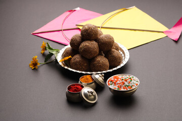 Til Gul OR Sweet Sesame Laddu with Kite model, haldi Kumkum and sugar crystals for Makar Sankranti festival over black background.